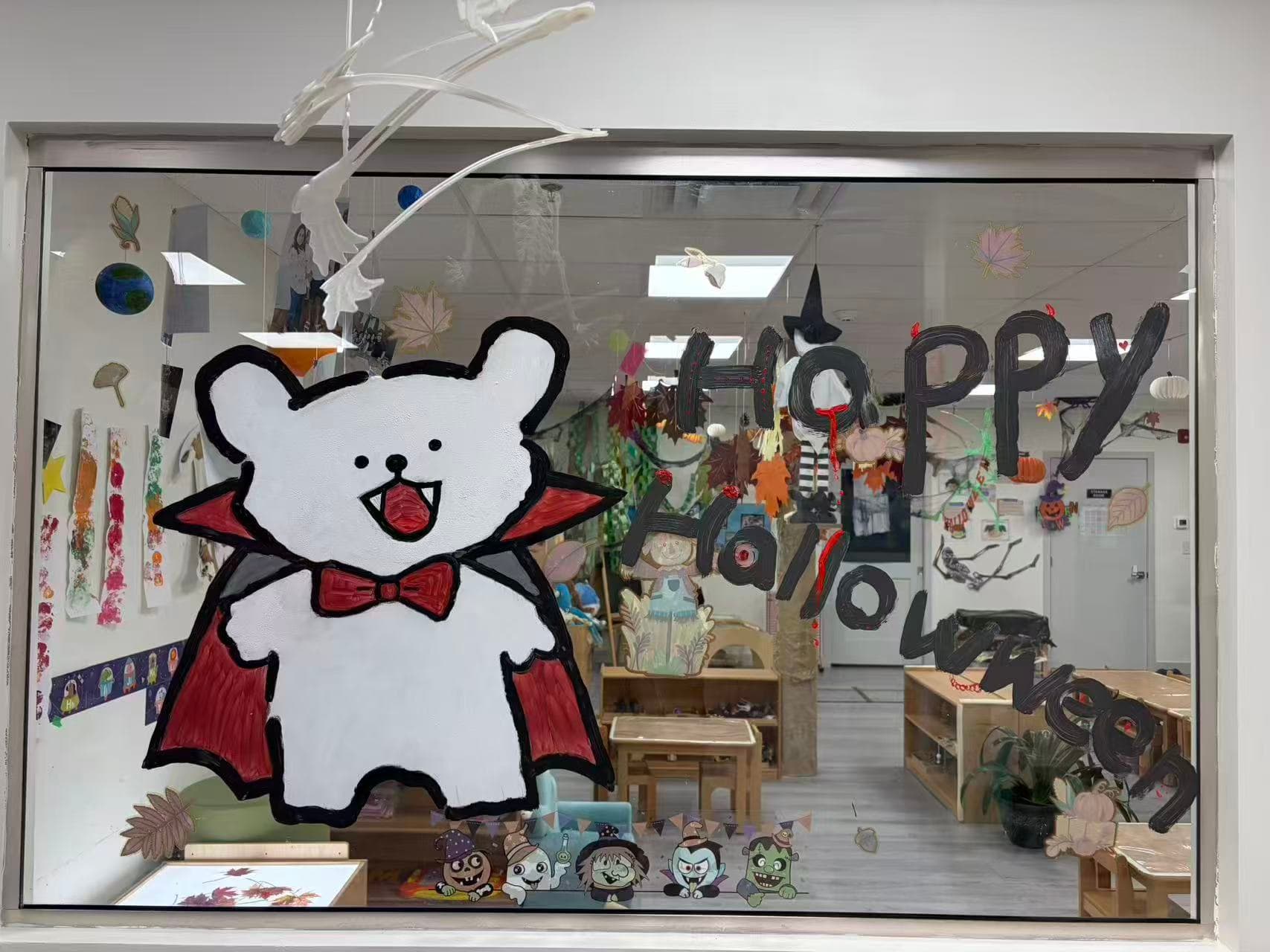 A classroom window painted for Halloween, looking in on child-sized tables and materials